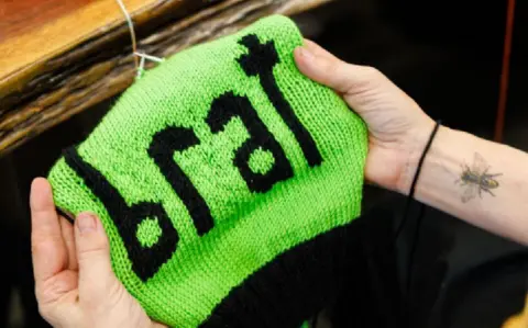 A green, knitted hat with the word brat on the front, made by Annette Corsino, owner of the Knitting Tree LA in California