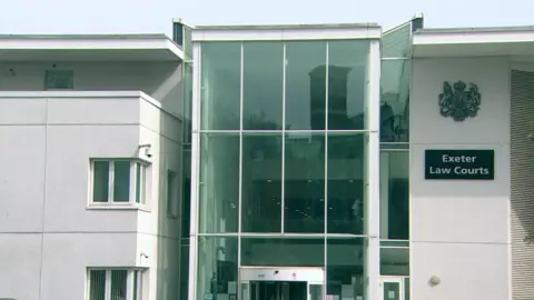 The front of the Exeter Crown Court building. There is a glass panel down the middle of the building and a sign on the right hand side which says 'Exeter Law Courts'.