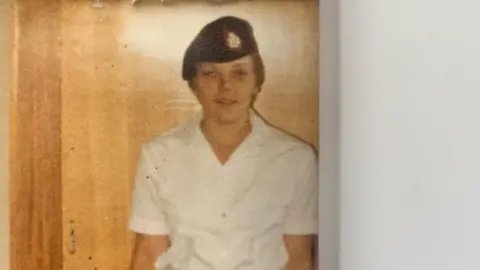 An old colour photo of a woman wearing a white shirt and army beret.