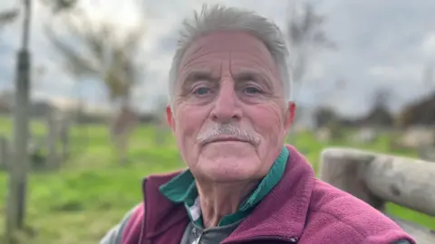 Chris Scroby, looking at the camera while sitting on a bench within the burial ground