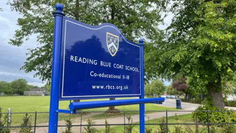 A blue sign reading Reading Blue Coat School - co-educational 11-18 with their web address underneath