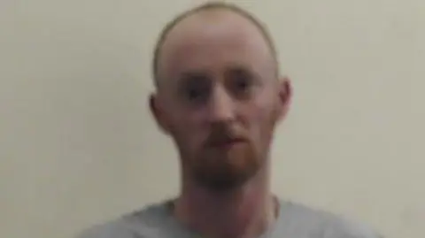 Police Scotland Blurry image of Christopher White in a grey T-shirt who is staring at the camera. He is balding and has a gingery beard.