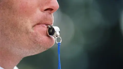 A man blowing a referee's whistle.