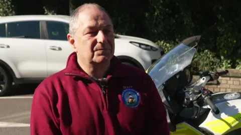 Steve Dower wearing a deep red fleece jumper. He is stood next to a motorcycle. 