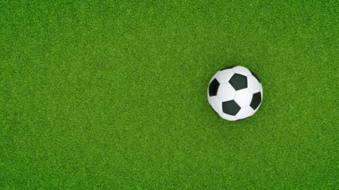 Getty Images A black and white football on a bright green artificial pitch.