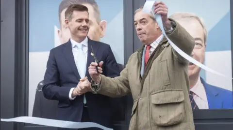 PA Media Reform leader Nigel Farage cuts a blue tape as he opens the party's campaign headquarters in Denton