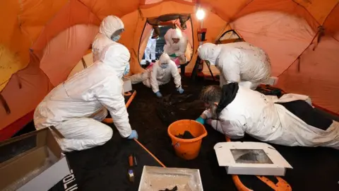 Men in forensics suits checking human remains