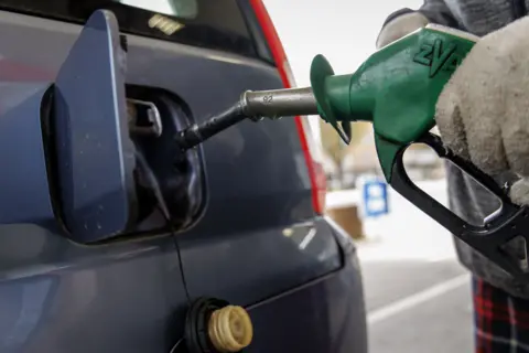 EPA/Shutterstock A gloved hand holding an unleaded petrol pump, putting petrol into a blue car