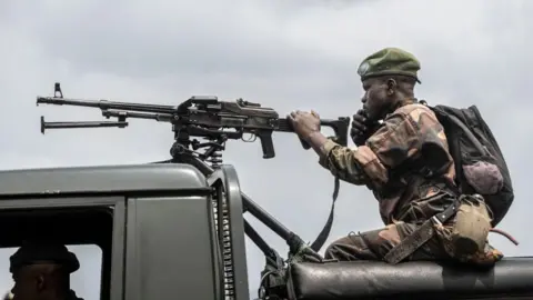 AFP via Getty Images A soldier from the Armed Forces of the Democratic Republic of Congo (FARDC) holds on to a mounted machine gun speaks on the phone along the road leading to the entrance of the town of Sake, in January 2025. 