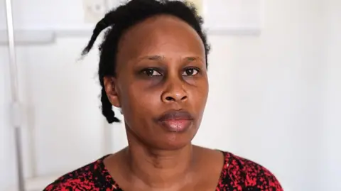 Barbara "Barbie" Kyagulanyi, in a red and green print dress, shows her bruised eye while resting on a hospital January 24, 2026 i