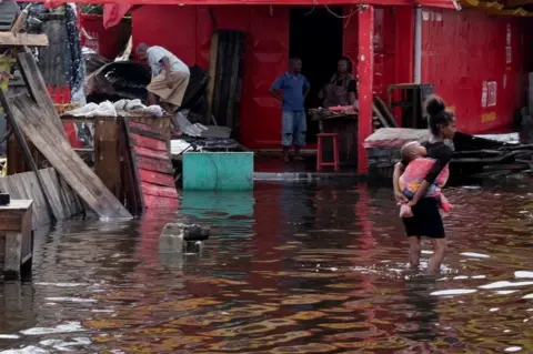 Reuters A girl carries an infant as she wades through water.
