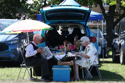 Reuters A couple sitting at a table outside their car eating lunch on a table with a tablecloth on it.