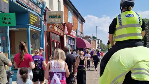 Hollie Gazzard Trust People walking down a road, with mounted police riding alongside them