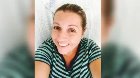 Handout Ali Alcock is smiling in this selfie taken as she lies on a hospital bed. She is wearing a mint green and blue striped T-shirt.