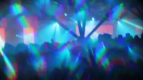 An abstract image shows the silhouette of people dancing inside a nightclub with multi-coloured lights and lasers shining.