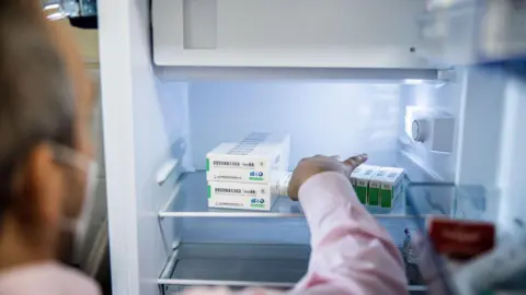 A medical worker removes a box of vaccines from a refrigerator.
