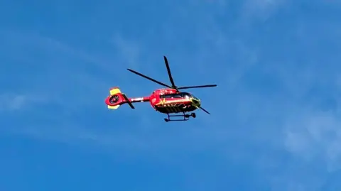 A red and yellow helicopter flying in the blue sky 