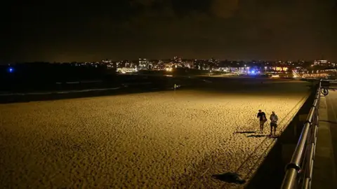 Getty Two people walk on a dark, empty beach