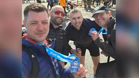 PJ Farr Four men smile at the camera in a selfie. Two are holding their medals which are blue and say Surrey Half Marathon on them