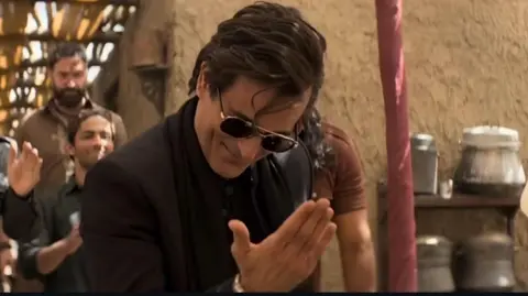 A scene from Dhurandhar in which Bollywood actor Akshaye Khanna, dressed in all black, is saluting people in a brick room while grooving to the music