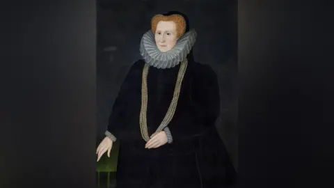 National Trust Images/John Hammond Portrait of Bess of Hardwick, who has ginger hair, a white ruff and a gold beaded chain against a black background.
