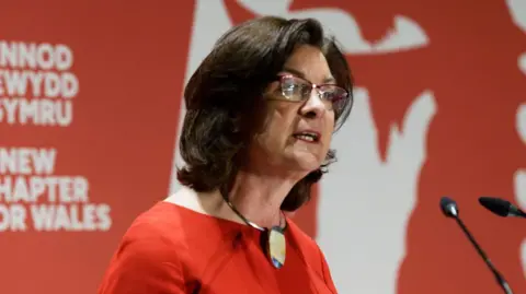 Athena Eluned Morgan addresses the audience at the Swansea launch event of Welsh Labour's manifesto. She is wearing red and stood at a podium