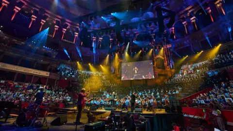 Musik untuk Kaum Muda Sebuah gedung konser besar dengan lampu warna-warni diisi oleh orkestra besar 