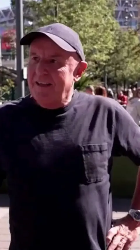 Older man wearing a hat and black t-shirt.