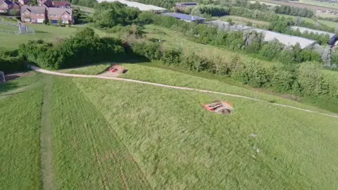 Andrew Wakeley/RWB Environment Trust An aerial image of a grassy area surrounded by trees and houses in the distance.