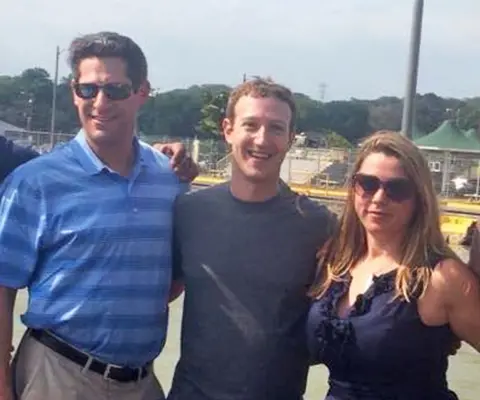 Joel Kaplan, Mark Zuckerberg e Sarah Win-Win-Win-W-Win-Win-Win-Wyliams estão fora do sol. Eles têm suas armas nas costas um do outro enquanto representam. Joel Kaplan, um cabelo castanho com cabelos castanhos, está usando um azul claro e uma camisa polo de madeira horizontal escura. Ele está usando óculos de sol. Mark Zuckerberg tem cabelos de gengibre curto e está usando uma camiseta cinza. A Sara Win-Wyliums tem cabelos longos e marrons claros e está usando óculos escuros e uma blusa freelada azul marinha.