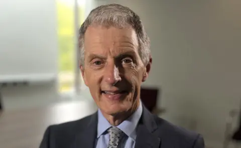 Martin Giles/BBC Prof David Maguire smiling at the camera. He is wearing a suit, a blue shirt and a tie