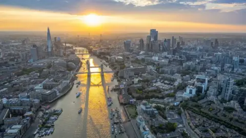 Sun sets over River Thames, showing Tower Bridge in foreground and Shard and City of London in background