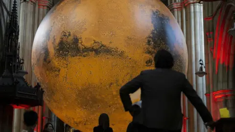 A large illuminated sculpture of the moon with the silhouette of a person in the foreground.