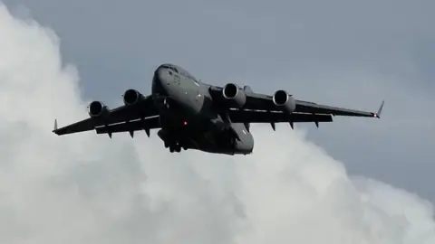  A large grey US Air Force military jet aircraft against a cloudy grey blue sky above a telegraph wire on Prestwick.