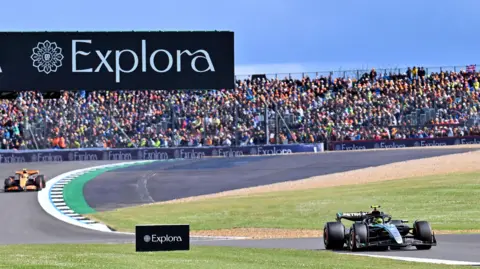 EPA Lewis Hamilton driving on Silverstone Circuit race track with rows and rows of fans dotted behind him. 
