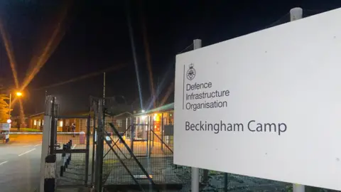 The sign outside Beckingham camp in the evening, with lights from the buildings flaring on the camera