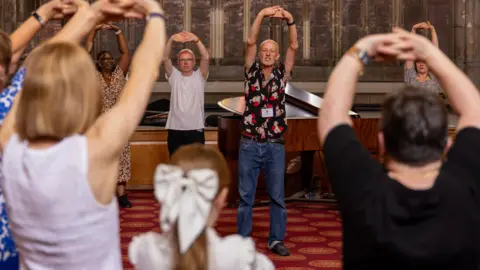 Dale Hodgetts A circle of people stood stretching their hands above their heads inside the cathedral.