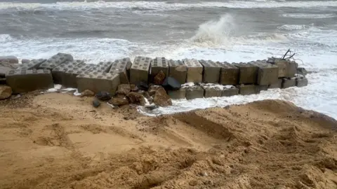 Richard Knights/BBC Dozens of large concrete blocks holding back big waves. The other side of the blocks is sand. 