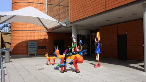 Colourful sculpture at the entrance of the Evelina Children's Hospital, with two orange four-legged animals and there are also sculptures resembling people around and on the animal sculptures. 