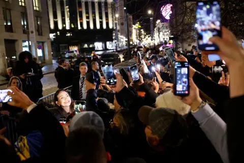 AFP via Getty Images Machado, whose face is illuminated by camera lights, smiles as supporters and media gather to see her arrival.