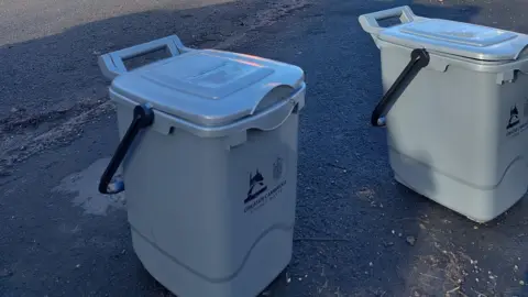 Greater Cambridge Shared Waste Grey bins are placed on a pavement.