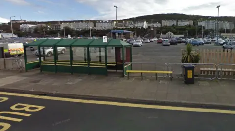 Cars parked in the empty lot behind a row of bus shelters and benches.
