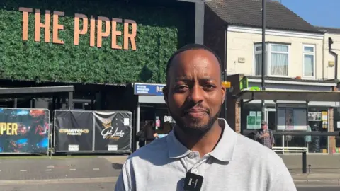 Reverend Peter Dua, wearing a grey polo shirt, in front of the former nightclub The Piper. The building still has The Piper sign on the front