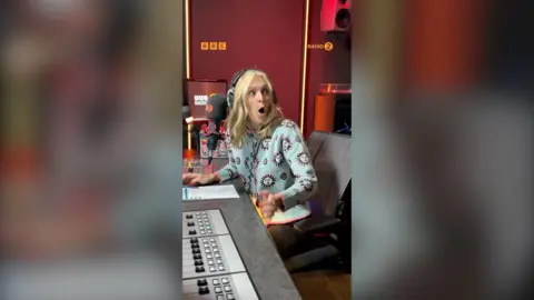 Fearne Cotton has a long blonde hair. She has her mouth open in surprise. She is a wearing a blue patterned cardigan.