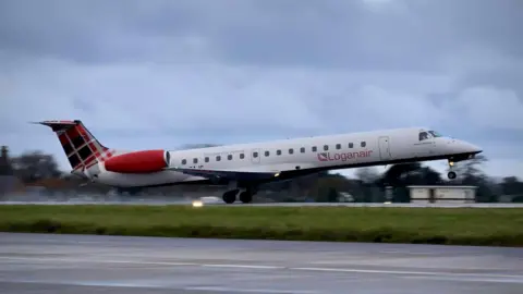 A Loganair plane takes off. Smoke from the rear tires can be seen. The front of the plane is in the air while the rear wheels are still grounded. The plane has a red tartan pattern on its fin. It is a cloudy day.