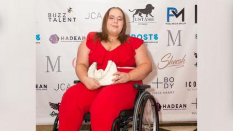 Caitlyn Payne sitting in a wheelchair in a red jumpsuit 
