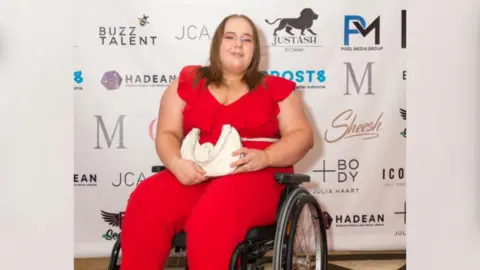 Caitlyn Payne sitting in a wheelchair in a red jumpsuit 