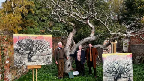 Dan Llywelyn-Hall Two men and a woman standing in front of the Bramley apple. 