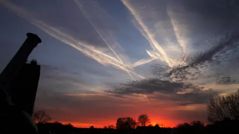 Getty Images A sky at dusk, with white contrails across the dark blue sky and a red sunset on the horizon