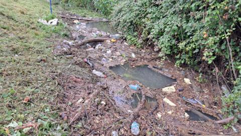 The brook filled with waste, including plastic bottles